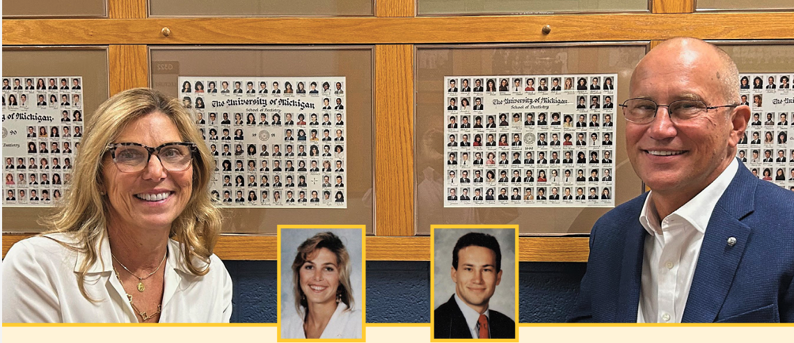 Middle-aged caucasian woman and man, both wearing glasses and smiling, stand in front of the class photos of dental alumni at the U-M School of Dentistry.